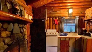 Interior acolhedor de uma cabana com lareira de pedra, fogão branco e bancada de madeira.