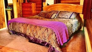 A wooden cabin bedroom with a bed, a dresser, and a window. - Rustic Log Cabin #6 - "Fireside" (Lisbon)