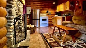 A cozy cabin interior with a stone wall, wooden ceiling, a kitchenette, and a sofa. - Rustic Log Cabin #6 - "Fireside" (Lisbon)