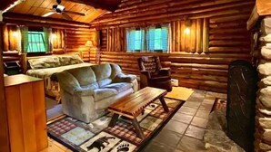 L'intérieur d'une cabane en rondins, avec un canapé, un fauteuil et une cheminée.