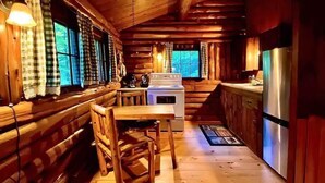 L’intérieur d’une cabane comprend une table à manger en bois, un banc et un coin cuisine équipé d’une cuisinière et d’un réfrigérateur.