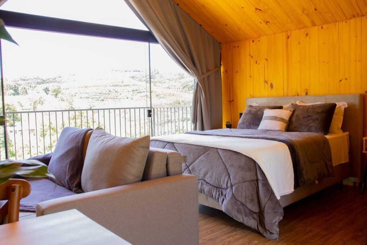 A bedroom with a bed, a sofa, and a balcony with a view.