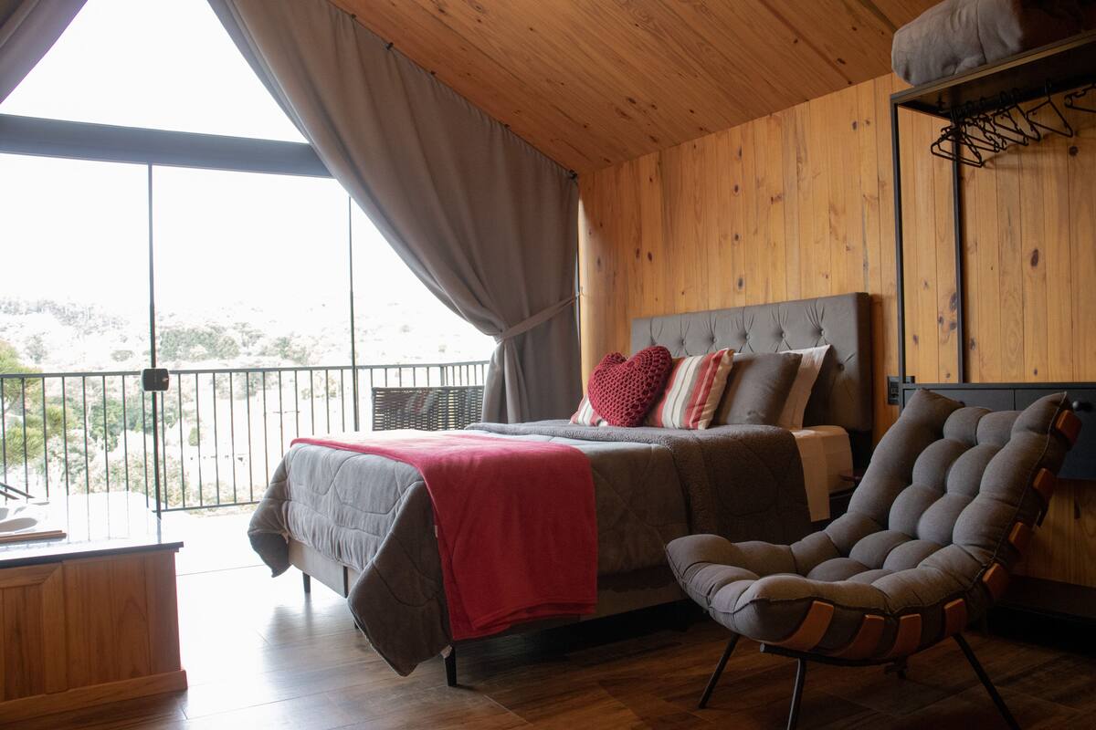 A bedroom with a bed, a chair, and a balcony with a view.