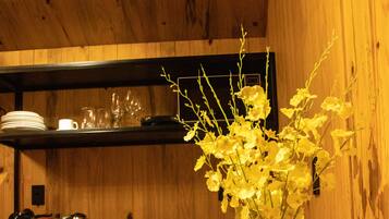Un interior de madera con una mesa, un jarrón con flores amarillas y utensilios de cocina en estantes.