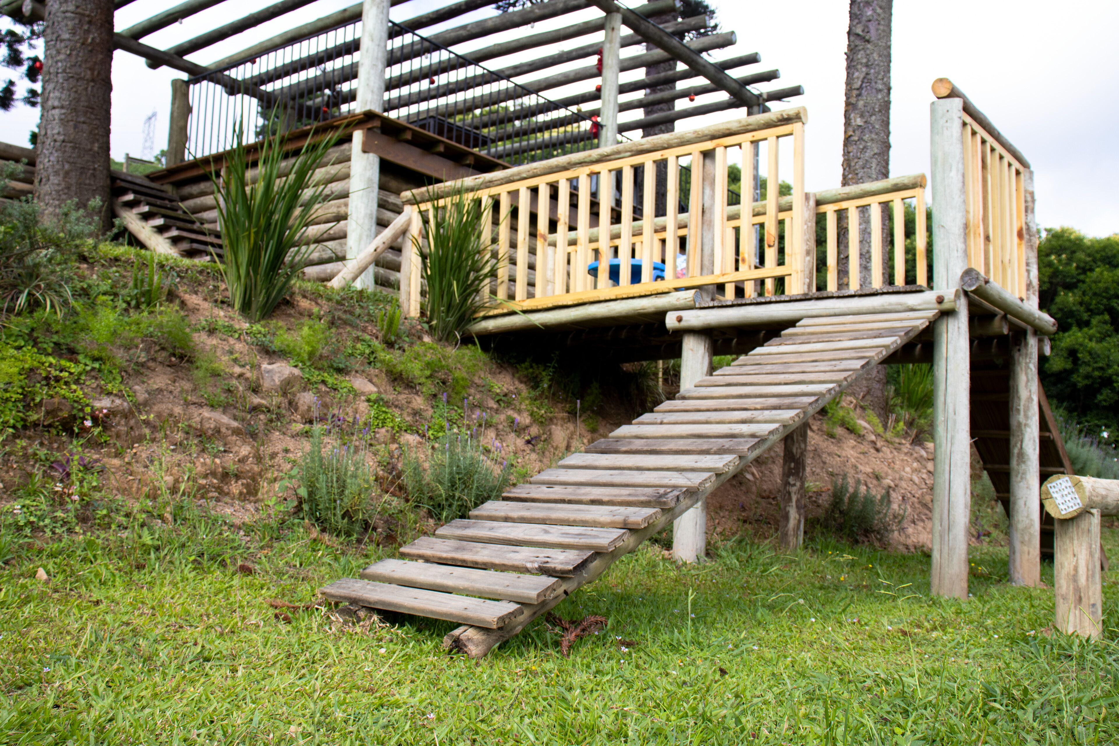 Un escalier en bois mène à une terrasse en bois agrémentée de rampes, le tout étant entouré de pelouse et de plantes.