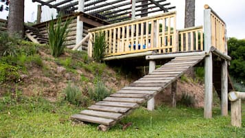 Un escalier en bois mène à une terrasse en bois agrémentée de rampes, le tout étant entouré de pelouse et de plantes.