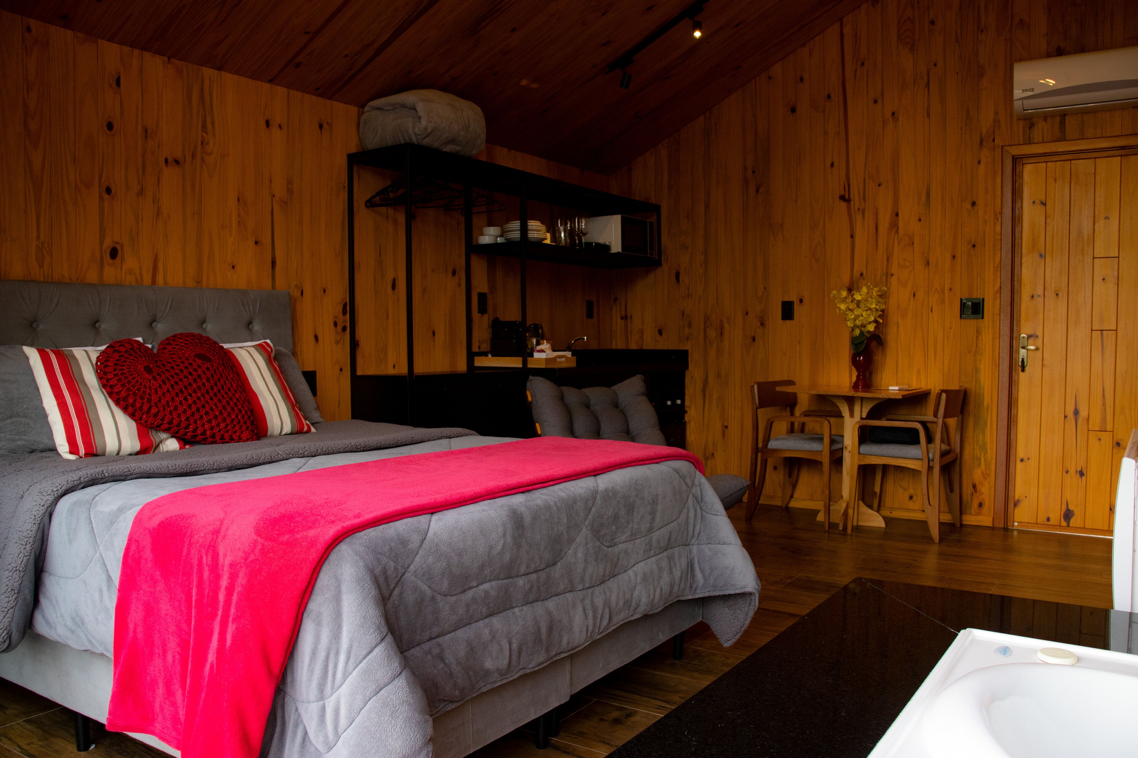 Quarto com cama, mesa de cabeceira, cadeira, parede de madeira e porta.