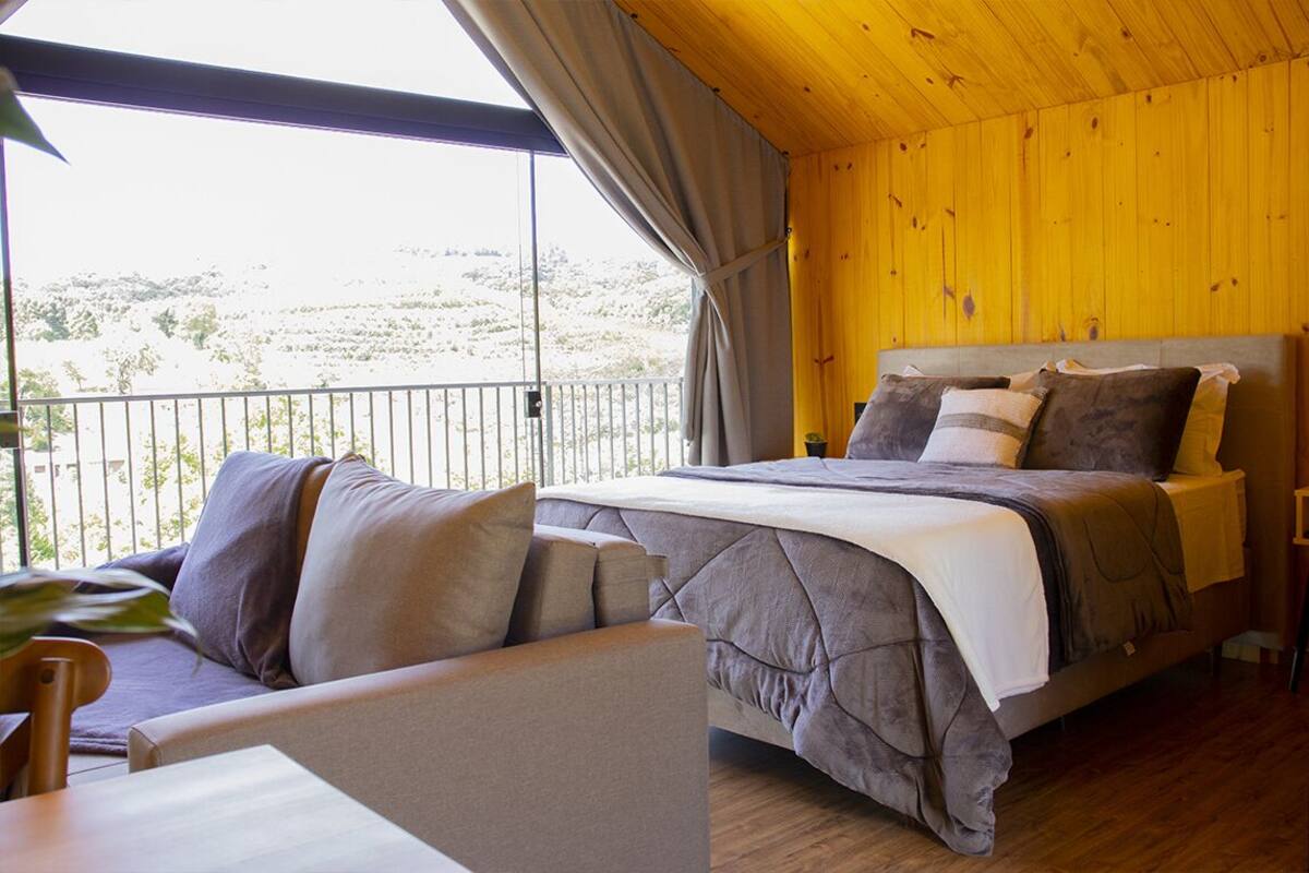 A bedroom with a large bed, a sofa, and a balcony with a view of the landscape.