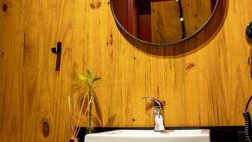 Een badkamer met een houten wand, een ronde spiegel, een wit wastafelmeubel en een handdouche, inclusief een handdoekhouder.
