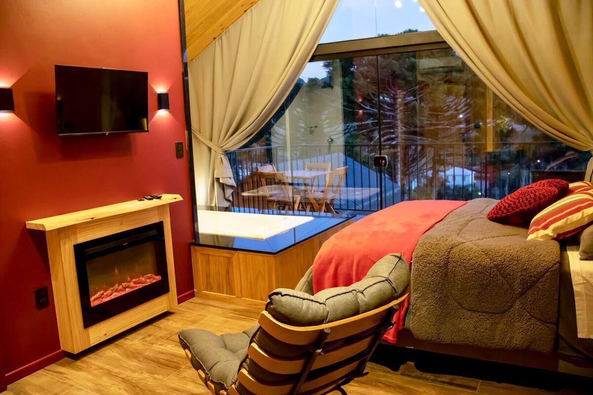 A bedroom with a bed, a chair, a fireplace, a TV, and a window with curtains.