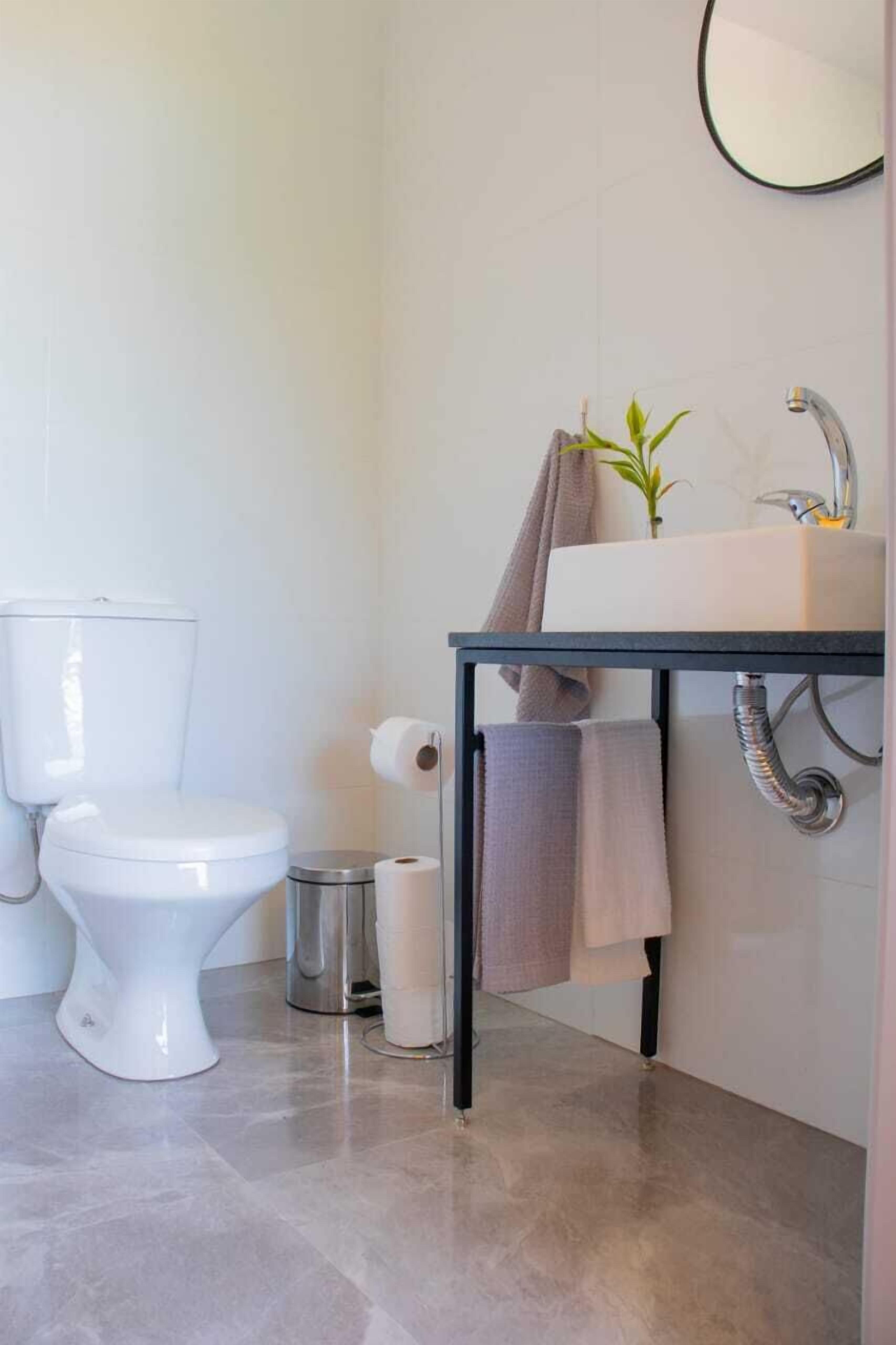 Uma casa de banho moderna com sanita, lavatório e um pequeno contentor de lixo.