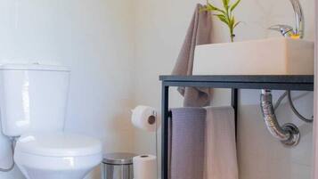 Uma casa de banho moderna com sanita, lavatório e um pequeno contentor de lixo.