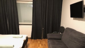 Une pièce comprenant un lit, un canapé, une télévision et une fenêtre avec des rideaux.