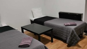Une petite pièce simple, avec deux lits, une petite table et un buffet noir.