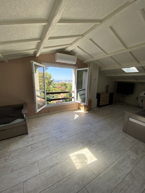 Una camera spaziosa con un ampio balcone, un letto, una TV e una ventola a soffitto.