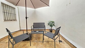 Ein kleiner Patio-Bereich mit Tisch und vier Stühlen, einem Blumentopf und einem großen Sonnenschirm.