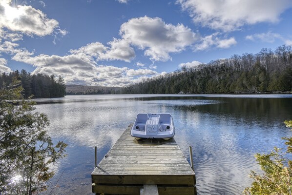 A boat docked at a wooden pier extending into a calm lake, surrounded by trees and a clear sky. - Chalet en Bois Rond Avec Spa, Sauna et Hammam (Labelle)