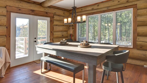 A log cabin dining area with a large wooden table, benches, and a chandelier. - Chalet en Bois Rond Avec Spa, Sauna et Hammam (Labelle)