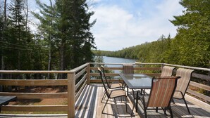 A wooden deck with a glass table and chairs, overlooking a lake and surrounded by trees. - Chalet en Bois Rond Avec Spa, Sauna et Hammam (Labelle)