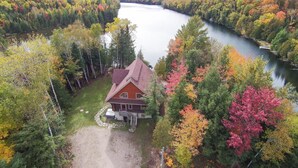 A cabin surrounded by autumn foliage, a lake, and a forested area. - Chalet en Bois Rond Avec Spa, Sauna et Hammam (Labelle)