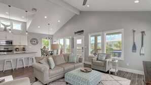 A spacious living area with a sofa, ottoman, and a kitchen in the background. - Paradise Vibes- Pond Views | 2 Balconies (Port Aransas)