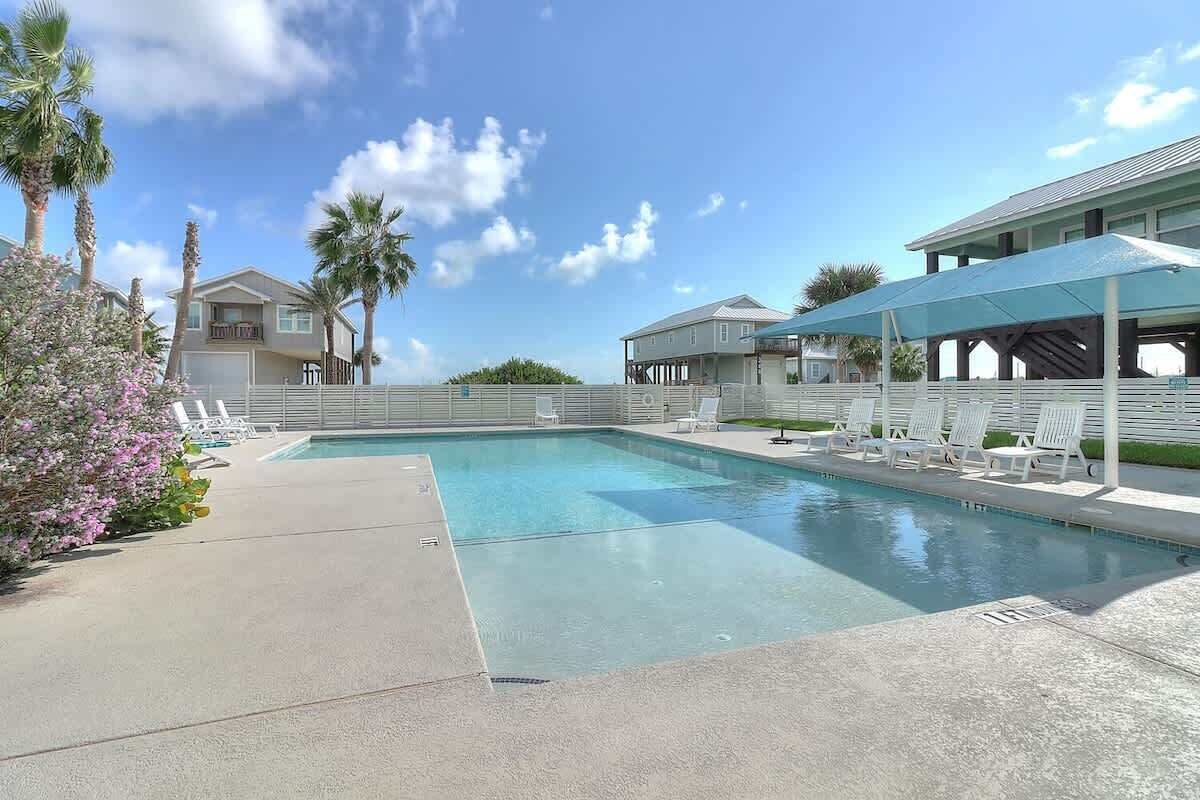 A swimming pool with lounge chairs, a covered area, and a building with a balcony.