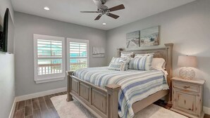 A bedroom with a bed, a ceiling fan, a nightstand, a lamp, and a window with blinds. - Paradise Vibes- Pond Views | 2 Balconies (Port Aransas)