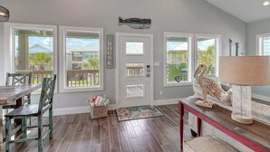 A spacious room with a dining area, a door with a 'HOUSE' sign, and a view of the outside. - Paradise Vibes- Pond Views | 2 Balconies (Port Aransas)