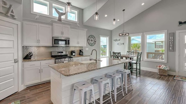 A spacious kitchen with white cabinetry, a large island with bar stools, and pendant lighting. - Paradise Vibes- Pond Views | 2 Balconies (Port Aransas)