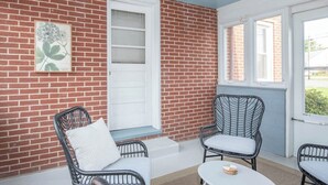 Une terrasse couverte, meublée de meubles en osier, avec une porte blanche et un mur en briques.