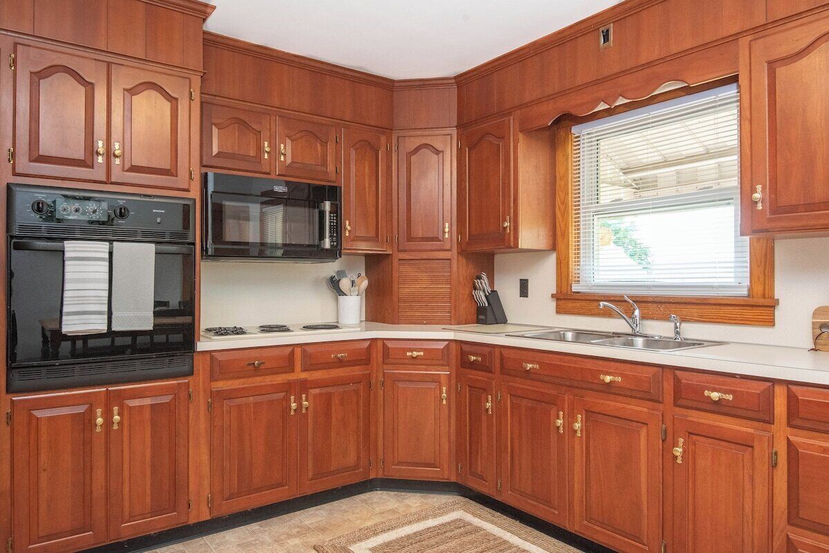 A kitchen with wooden cabinets, a stove, a microwave, and a window with blinds.