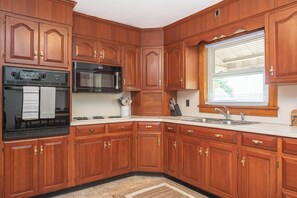 A kitchen with wooden cabinets, a stove, a microwave, and a window with blinds.