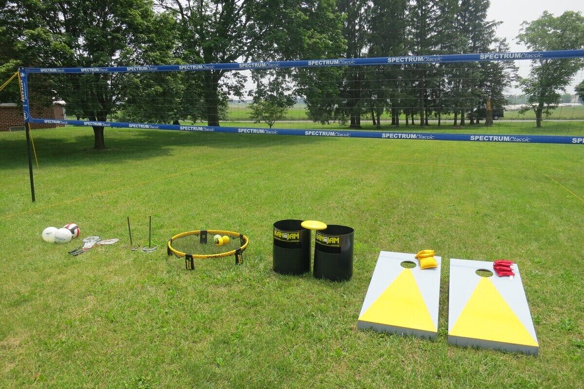 A grassy field with a blue net, two black barrels, a yellow hoop, and two triangular targets.