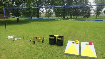 A grassy field with a blue net, two black barrels, a yellow hoop, and two triangular targets.