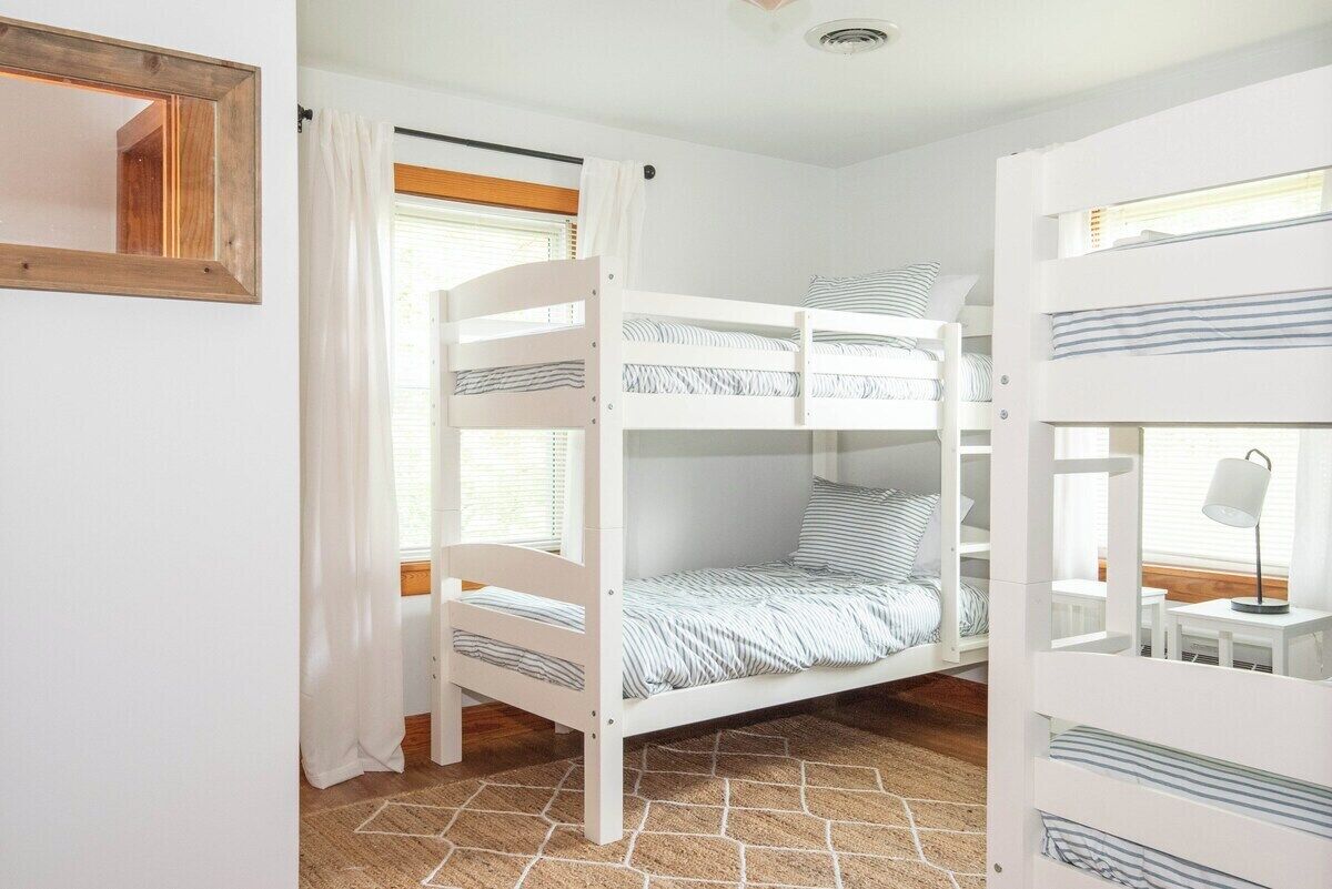 Ein Schlafzimmer mit Etagenbetten, einem Spiegel, Vorhängen und einem kleinen Tisch mit Lampe.