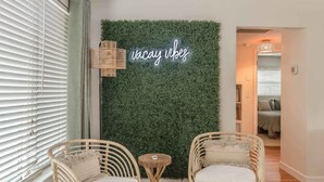 A room with two wicker chairs, a small round table, and a neon sign that reads "vacay vibes" against a green wall. - Relaxed 3BR retreat w/ heated pool & patio (Clearwater)
