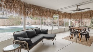 A sunroom with a pool, a black sectional sofa, a dining table with chairs, and a ceiling fan. - Relaxed 3BR retreat w/ heated pool & patio (Clearwater)