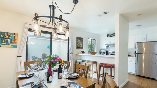 A dining area with a wooden table set for a meal, a chandelier, and a kitchen in the background.
