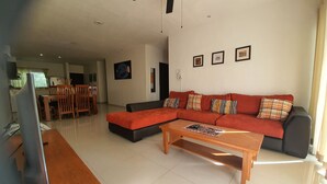 A living room with a sectional sofa, a wooden coffee table, and a ceiling fan. There is a dining area with a table and chairs in the background. - Luxury and Boutique Apartment by Bookhap (Playa del Carmen)