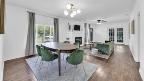 Un salon moderne comprenant un coin repas, un plancher en bois, des chaises vertes, une cheminée et un ventilateur de plafond.