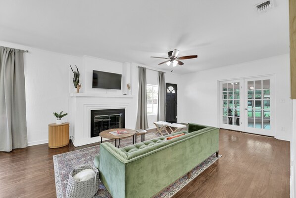 A living room with a green sofa, a fireplace, a ceiling fan, and a large window. - Comfy beds, Game Room, & Clean - Worth it! (Weslaco)