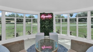 Une pièce avec une table en verre, deux coins salon avec des fauteuils confortables, un panneau néon sur lequel on peut lire « restez éveillé(e) », et une vue sur une pelouse verdoyante à travers de grandes fenêtres.