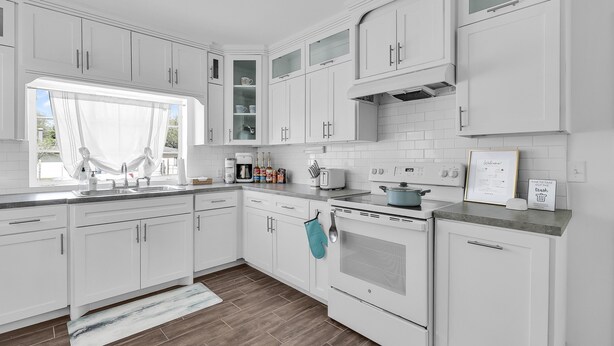 Une cuisine moderne avec des meubles blancs, une grande fenêtre et un plancher en bois.