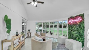 Un salon moderne doté d’une grande fenêtre, d’un ventilateur de plafond, d’un néon et d’un mur vert.