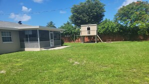 Un jardin à l’arrière d’une maison, avec une maison, un patio couvert et une petite construction en bois.