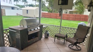 Un patio abrité avec un barbecue, une chaise et une vue sur le jardin.
