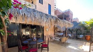 An outdoor patio with a round table and chairs, a thatched roof, and a view of a building with balconies. - Authentic 3-story Mexican Villa with Rooftop Views - 5 min from the beach! (El Pescadero)