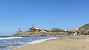 A coastal building with a prominent tower, situated on a beach with a rocky shoreline and a clear blue sky. - Authentic 3-story Mexican Villa with Rooftop Views - 5 min from the beach! (El Pescadero)