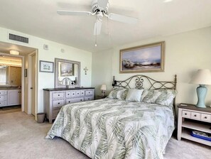 Quarto com cama, ventoinha no teto, um quadro, mesa de cabeceira e cômoda.