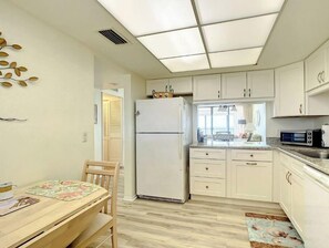 Cozinha compacta com armários brancos, geladeira, micro-ondas e área de refeições com mesa e cadeiras.